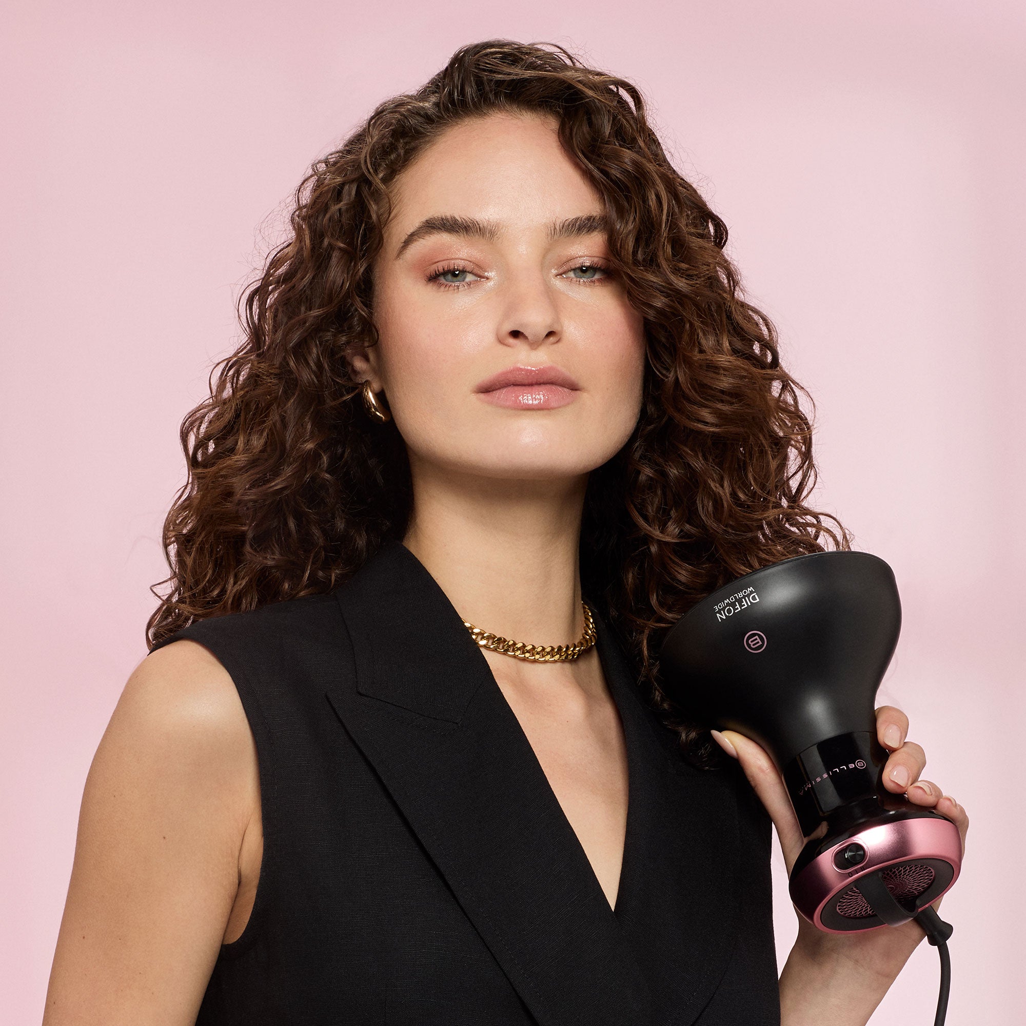 Woman holding a 2 in 1 Curly Hair dryer against a pink background